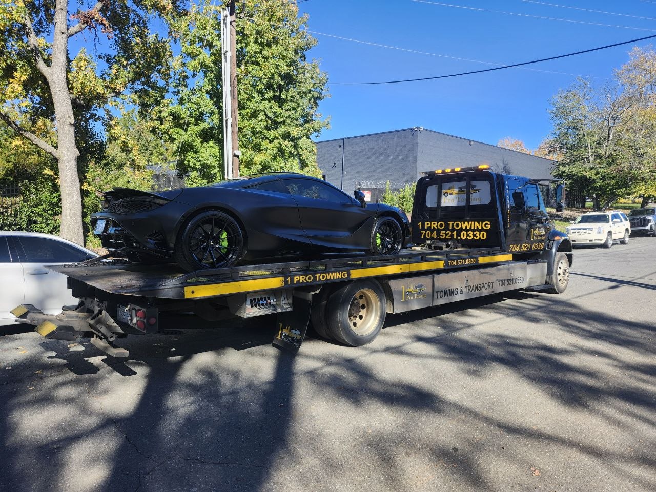 1 Pro Towing flatbed transporting a matte black McLaren supercar